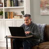Image of Man working on a laptop at a swivel TV tray table on the couch